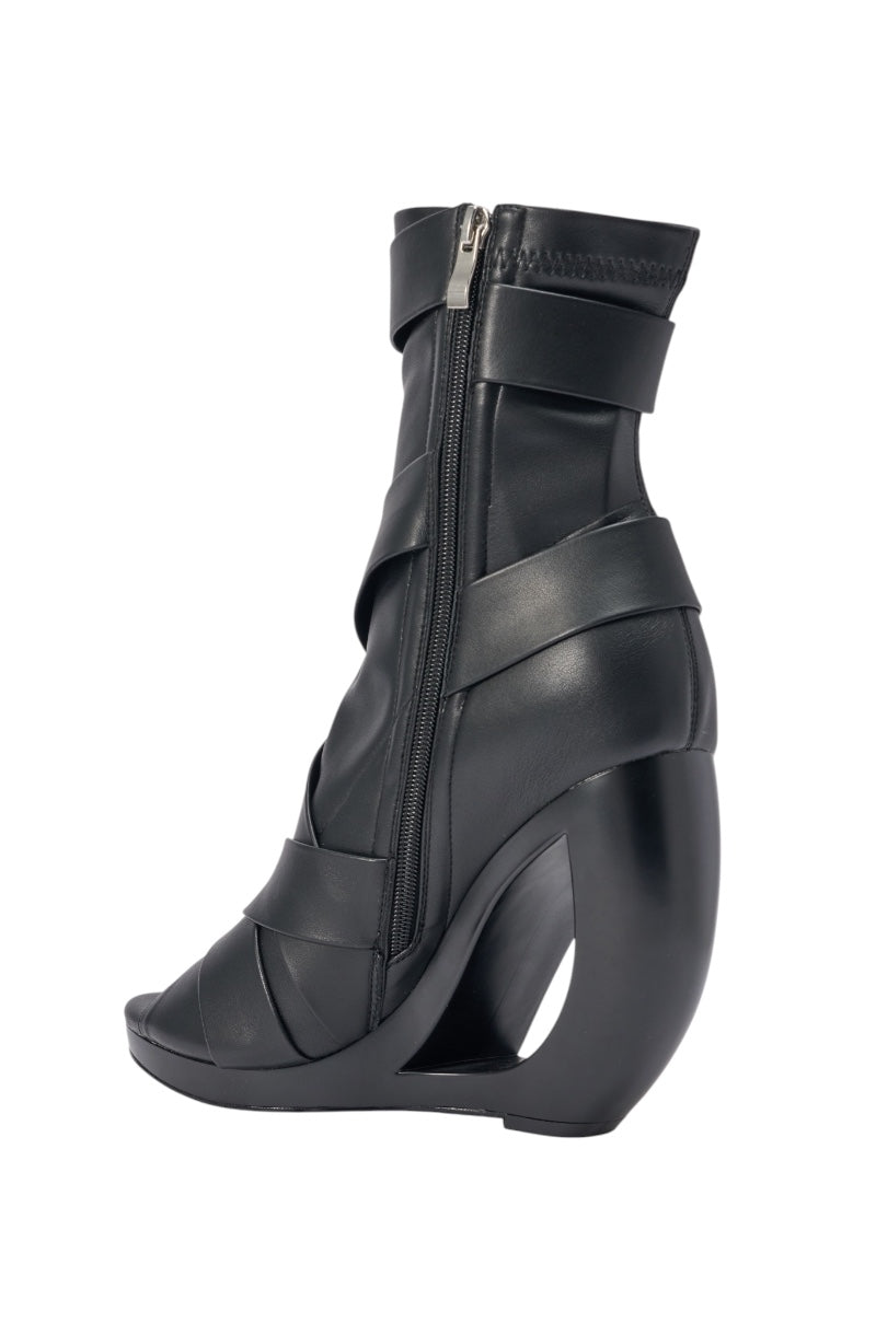 The AZALEA WANG IGNITE black wedge open toe bootie features belting detail, a sculpted empty wedge heel, wide faux leather straps, and a side zipper closure—this modern mid-calf bootie is distinctly avant-garde. 4