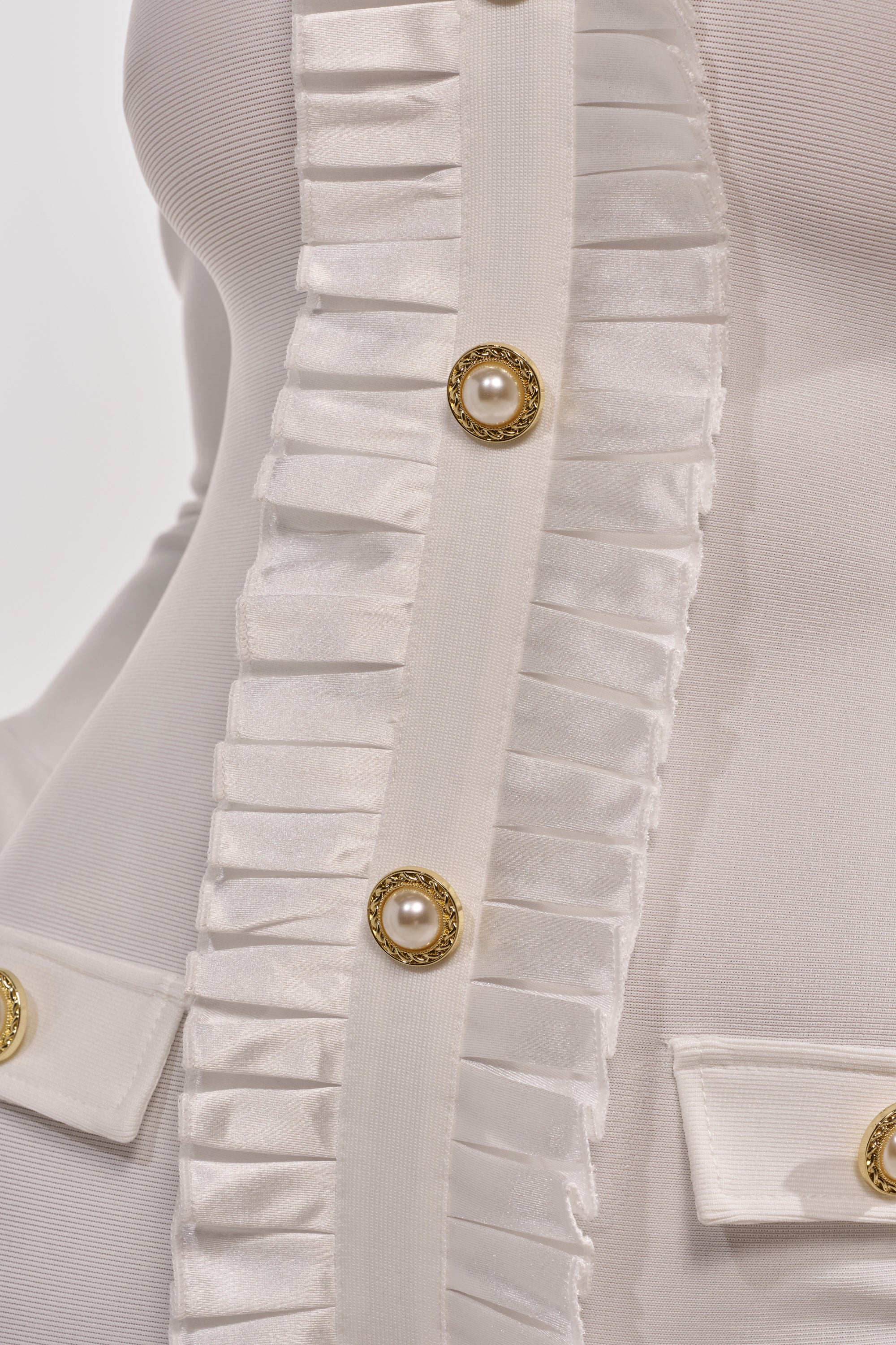 Close-up of the SAKURA Bandage Ruffle Mini Dress in white, featuring pleated satin ruffle trim, gold buttons with pearl centers, and two decorative pocket flaps. 12