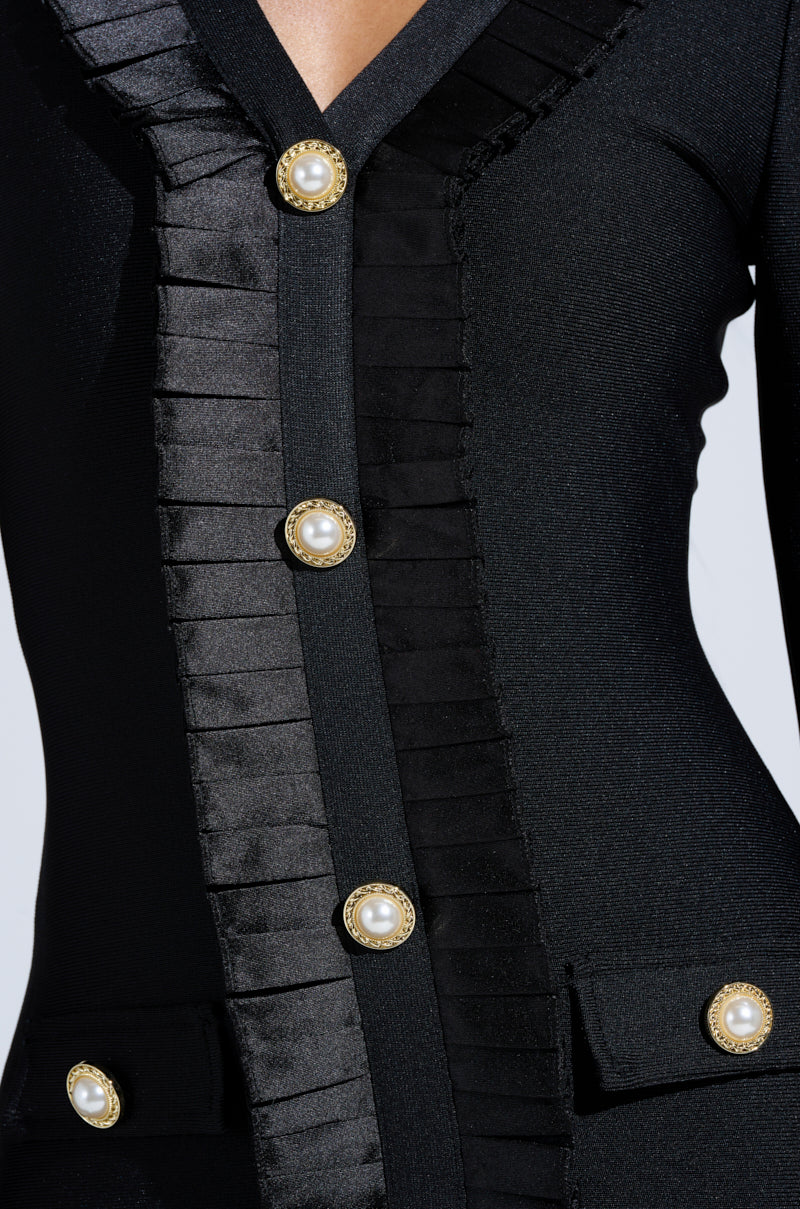 Close-up of the SAKURA BANDAGE RUFFLE MINI DRESS, a black mini dress with pleated satin trim, pearl-embellished buttons, flap pockets, textured details, and a deep V neckline.