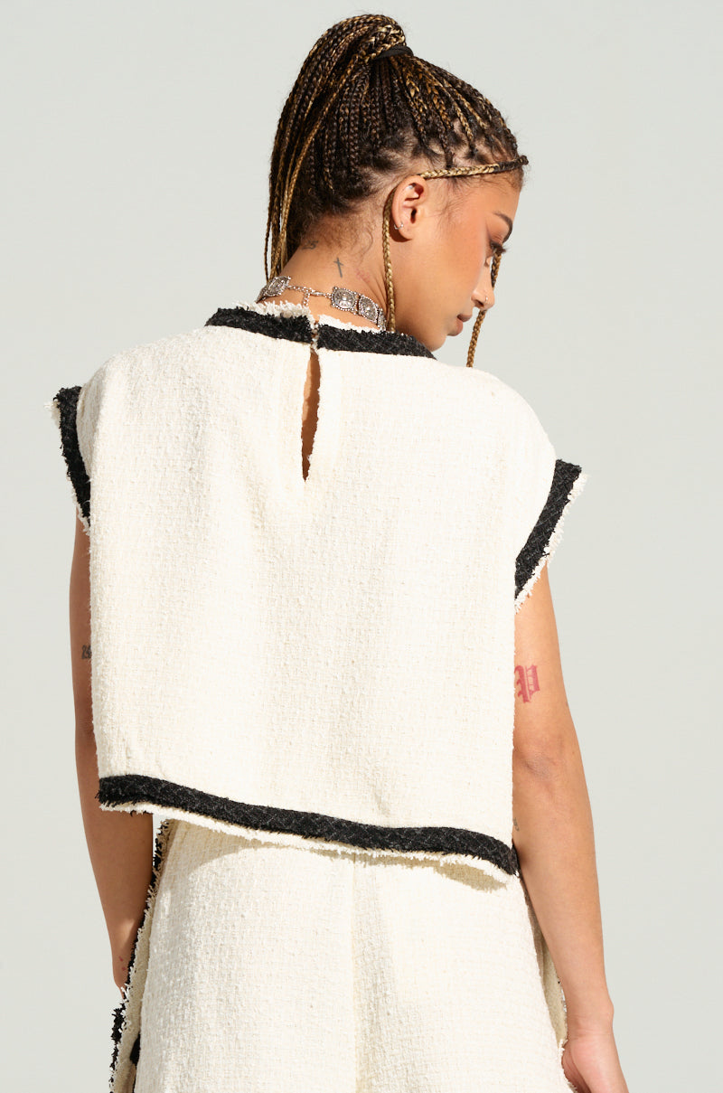 A person with braided hair is seen from the back, wearing the EVERYONES TYPE SHORT SLEEVE TOP. They accessorize with a silver necklace and have a visible tattoo on their upper left arm. The white top features black trim and a small slit near the neckline, while its cropped silhouette stands out against the plain light gray background. 4