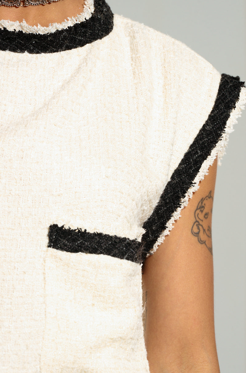 Close-up of a person's upper torso wearing the EVERYONES TYPE SHORT SLEEVE TOP, which is a sleeveless, textured tweed off-white shirt with black trim around the collar, sleeve edges, and pocket. A tattoo featuring a small character is visible on their upper arm. 6
