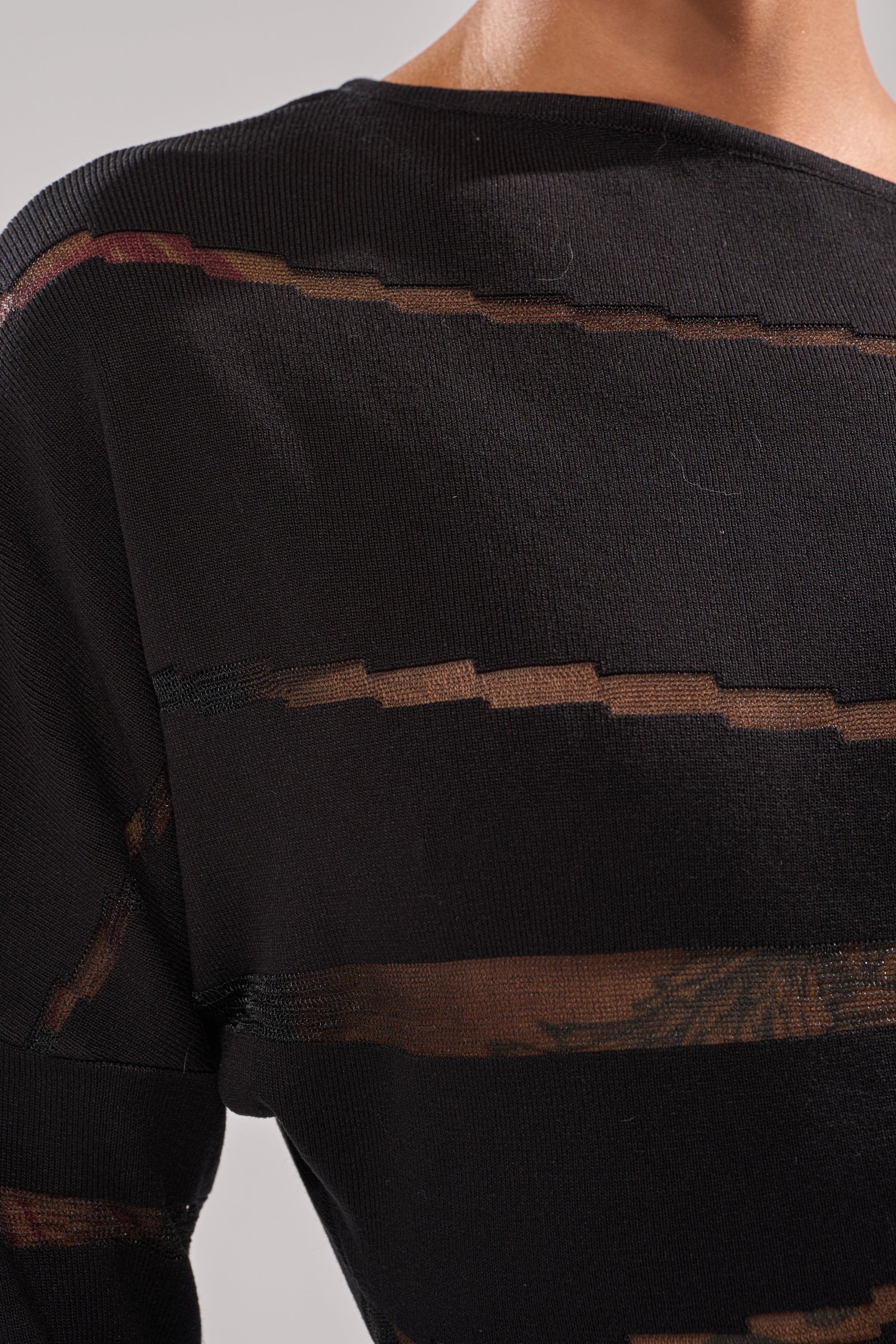 A close-up of a person's shoulder wearing the AFTER DARK STRIPED MINI DRESS, featuring sheer horizontal mesh stripes that reveal skin and a faint tattoo through the transparent sections.