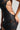 A person wearing the UP CLOSE AND PERSONAL MESH MINI DRESS—a black, distressed mesh mini dress featuring numerous cutouts that expose skin. The dress has thin straps and tightly hugs the individual's body, with a faux silver metallic zipper running down the back, adding an edgy touch. The person is holding the side of the dress with one hand, emphasizing its texture and design.