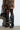 A person wearing a leopard print skirt and sheer thigh-high stockings stands in front of a white wall, sporting slouchy AZALEA WANG IMOGINE BLACK SNAP BOOTS. They hold a black handbag with ruffled details as shadows fall on the ground.