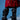 A person wears a shiny red coat and striking AZALEA WANG IMOGINE BLACK SNAP BOOTS—sculptural, knee-high with ruffled layers and a stiletto heel—while standing against a blue background.