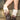 Wearing brown faux leather studded shorts and AZALEA WANG IMOGINE BROWN MULTI FOLDED DETAIL STILETTO BOOTS, a person stands against a brick wall and wire fence, with only their lower body visible.