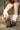 Wearing brown faux leather studded shorts and AZALEA WANG IMOGINE BROWN MULTI FOLDED DETAIL STILETTO BOOTS, a person stands against a brick wall and wire fence, with only their lower body visible.