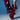 A person wears the AZALEA WANG IMOGINE BURGUNDY STILETTO SNAP BOOT—oversized, sculptural deep red leather with folds and metallic studs—against a blue background, highlighting the bold pointed toe stiletto style. Only the legs are visible.