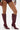 Wearing high-waisted dark purple vinyl shorts and AZALEA WANG IMOGINE BURGUNDY STILETTO SNAP BOOTS, a person stands against a plain white background.