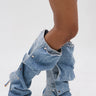 Person wearing the AZALEA WANG IMOGINE DENIM SNAP BOOT—knee-high, pointed toe, stiletto heel, crafted from slouchy blue denim with metal snap details—stands against a plain white background.