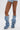 A person stands against a white background wearing light blue denim shorts and the AZALEA WANG IMOGINE DENIM SNAP BOOT—tall, slouchy denim boots with pointed toes, stiletto heels, and metal button details.