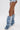 A person wears light denim shorts and the AZALEA WANG IMOGINE DENIM SNAP BOOT—slouchy denim boots with a pointed toe, stiletto heel, and silver snaps—standing against a plain white background.