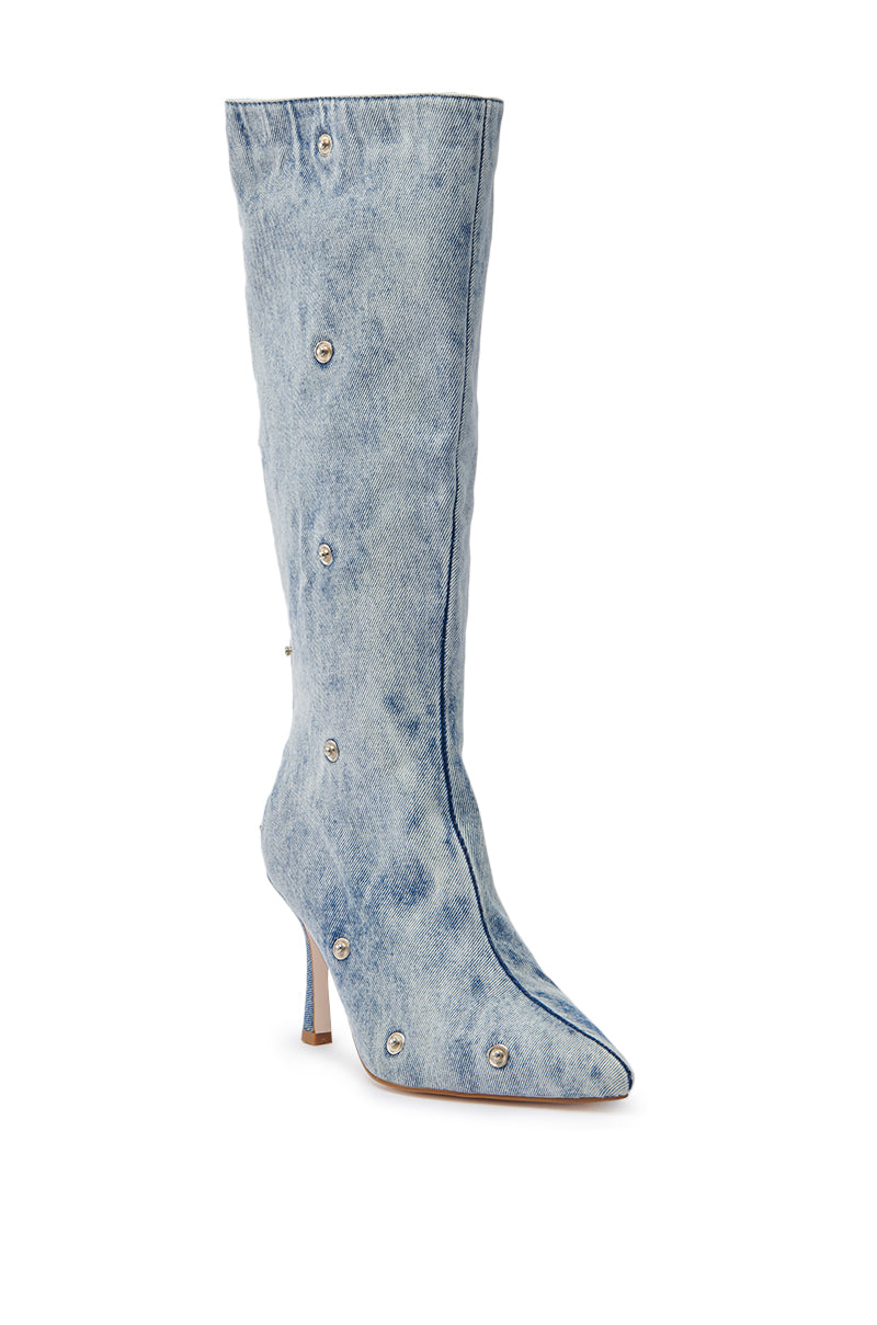 The AZALEA WANG IMOGINE DENIM SNAP BOOT is a knee-high, light blue denim boot with a pointed toe, stiletto heel, and bold decorative silver eyelets scattered across the surface.