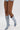 Wearing the AZALEA WANG IMOGINE DENIM SNAP BOOT—light blue, knee-high, pointed toe, stiletto heel with gold buttons—a person styles them with denim shorts and poses against a plain white background.