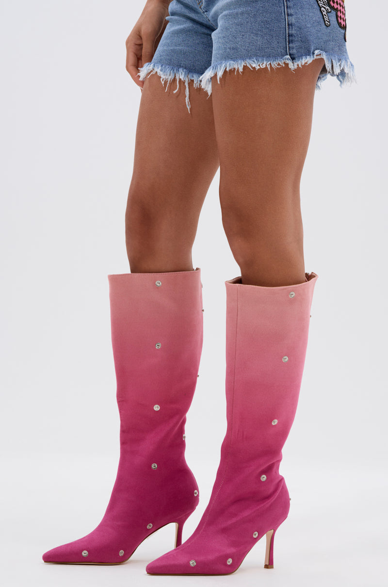 A person wears frayed denim shorts and the AZALEA WANG IMOGINE PINK MULTI FAUX SUEDE BOOT—knee-high ombré pink boots with pointed toes, stiletto heels, and small studs—standing against a plain white background.