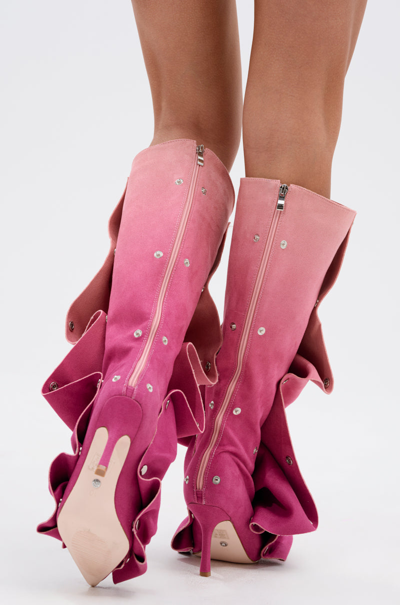 A person stands on tiptoe in AZALEA WANG IMOGINE PINK MULTI FAUX SUEDE BOOTS, featuring an ombré gradient from light to dark pink, ruffled details, silver studs, stiletto heels, and back zippers.