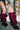 A person in a floral embroidered jacket and denim shorts adjusts AZALEA WANG IMOGINE PURPLE OMBRE FOLDED DETAIL STILETTO BOOTS while standing indoors on a textured floor in front of glass blocks.