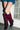 A person in a short denim skirt and AZALEA WANG IMOGINE Purple Ombre Folded Detail Stiletto Boots stands with legs crossed near a glass block wall.