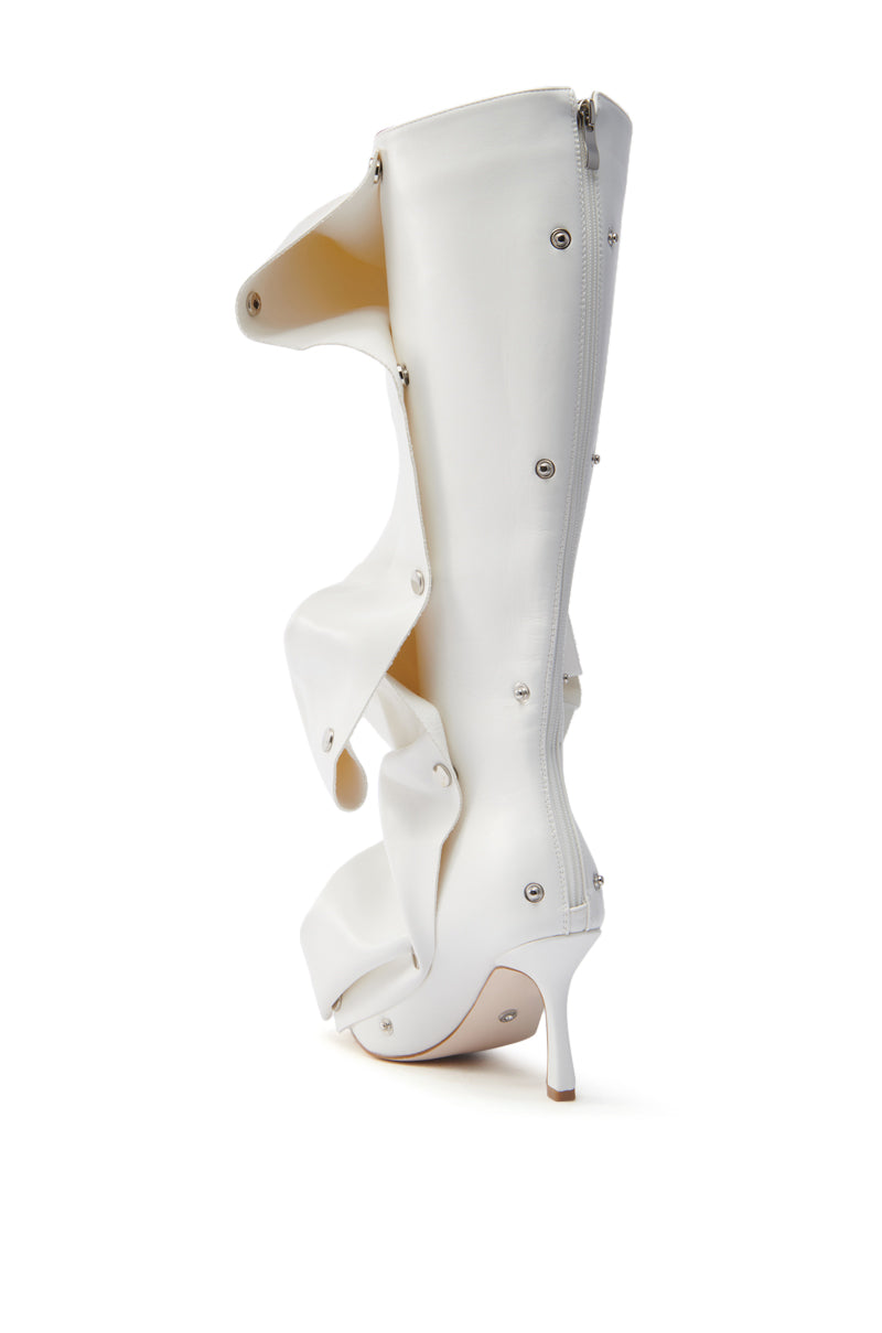 The AZALEA WANG IMOGINE WHITE BOOT is a knee-high faux leather boot with a distinct abstract design, featuring layered flaps, silver rivets, a side zipper, and a slender low heel against a plain white backdrop.