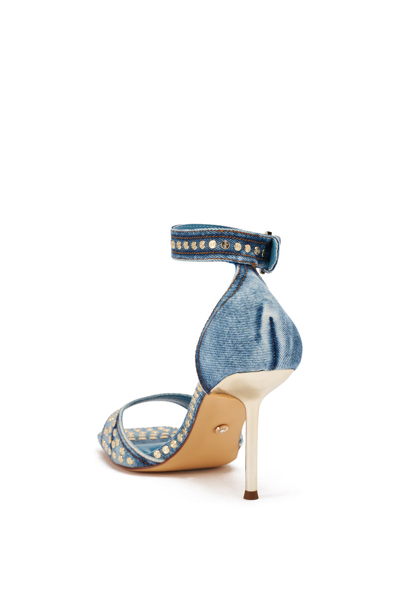 The AKIRA GOLD INANA DENIM STUD EMBELLISHED STILETTO SANDAL features blue denim, gold studs, a stiletto heel, ankle strap, and beige sole, displayed from the back on a white background. 5