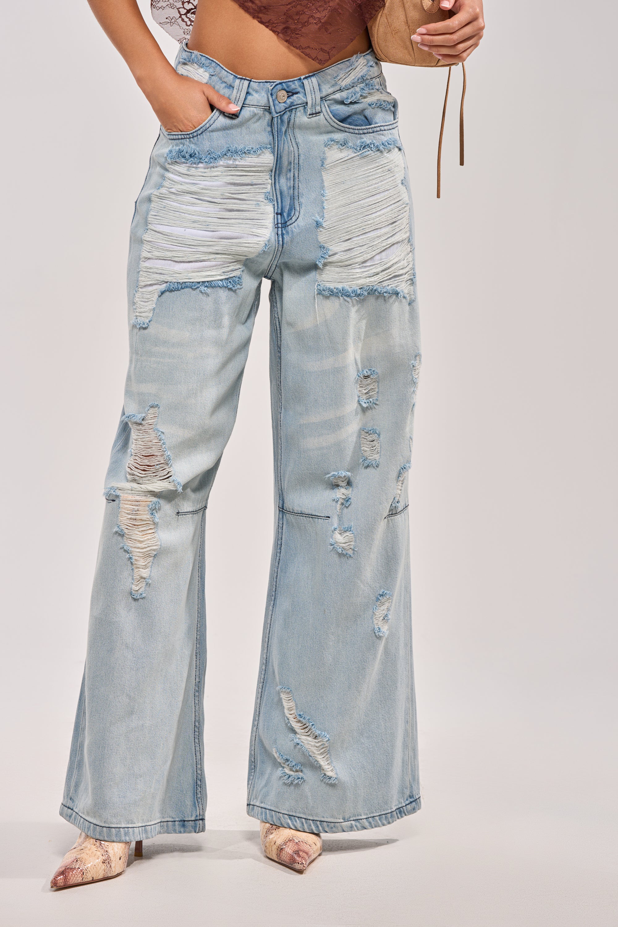 Wearing SUPER DISTRESSED WIDE LEG DENIM in a light wash with heavy fraying, styled with pointed-toe snakeskin shoes and a tan purse, this outfit features the baggy jeans trend; the upper body is partially out of frame. 1