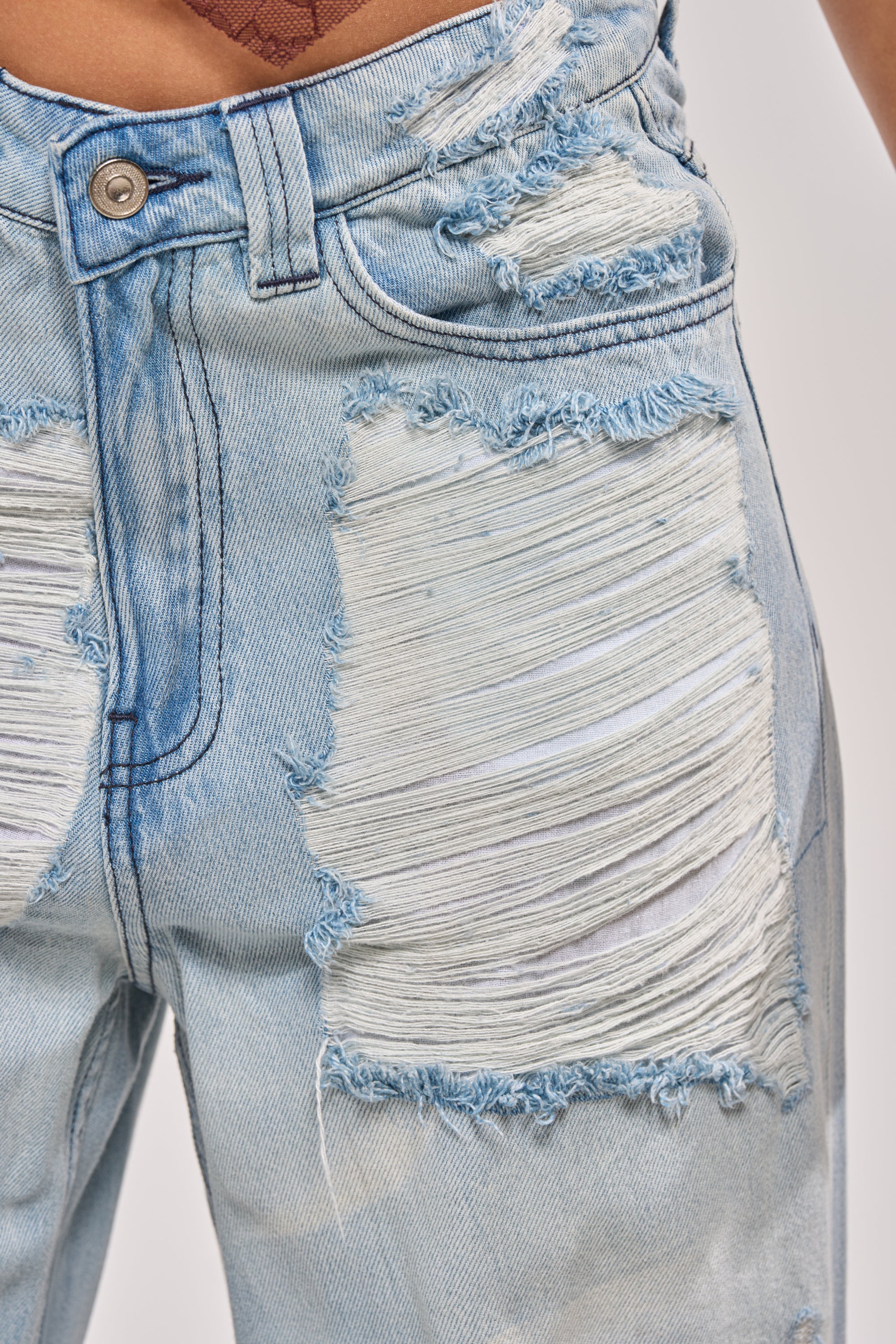 Close-up of SUPER DISTRESSED WIDE LEG DENIM in light blue, featuring large frayed horizontal rips and exposed white threads on the front thighs, with a visible metal button and waistband at the top. 7