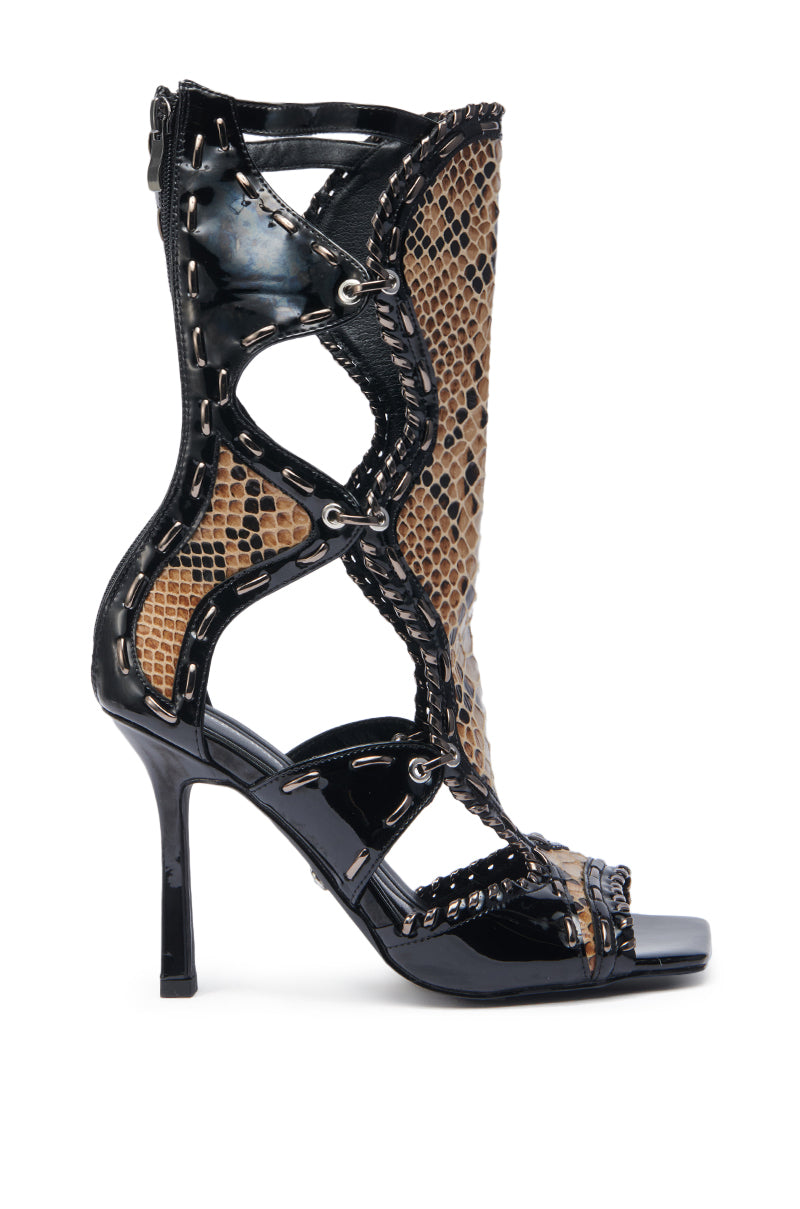 The AZALEA WANG INDRANI BLACK GLADIATOR SANDAL is a high-heeled, open-toe lace-up boot with a stiletto heel, black patent leather trim and sole, plus brown and black snakeskin-embossed upper with cutout sides.