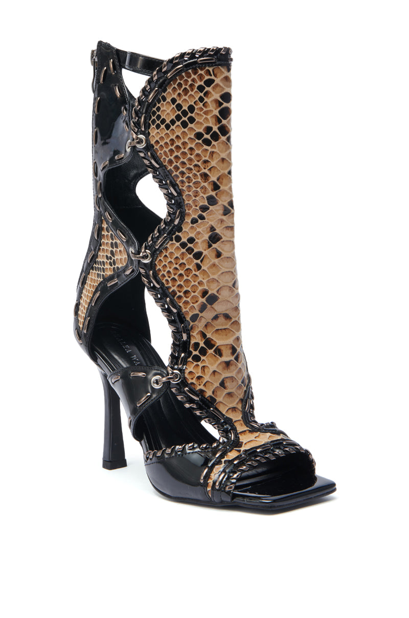 The AZALEA WANG INDRANI BLACK GLADIATOR SANDAL features a high heel, open toe, black sole and heel, tan and black snakeskin-embossed panels, cutout sides, and silver eyelet accents for a bold, fashion-forward look.