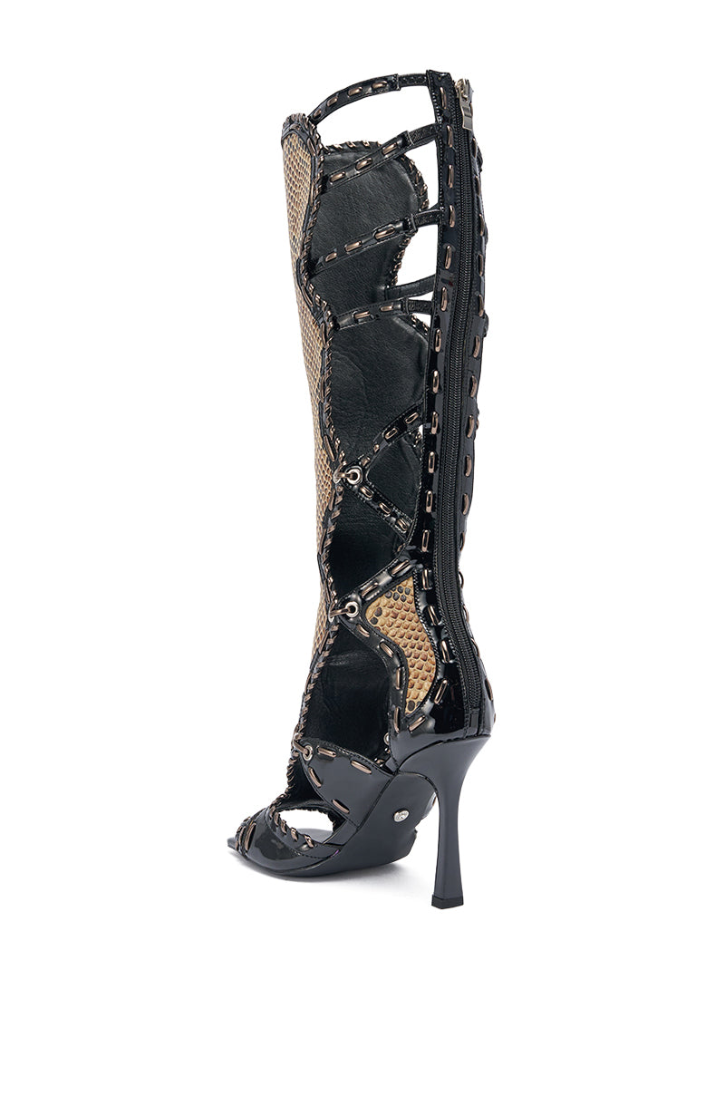 The AKIRA GOLD INDRANI BLACK HIGH SHAFT GLADIATOR SANDAL is a knee-high, open-toe stiletto in faux patent leather, with cut-outs, snake-patterned panels, and metal eyelets. 10