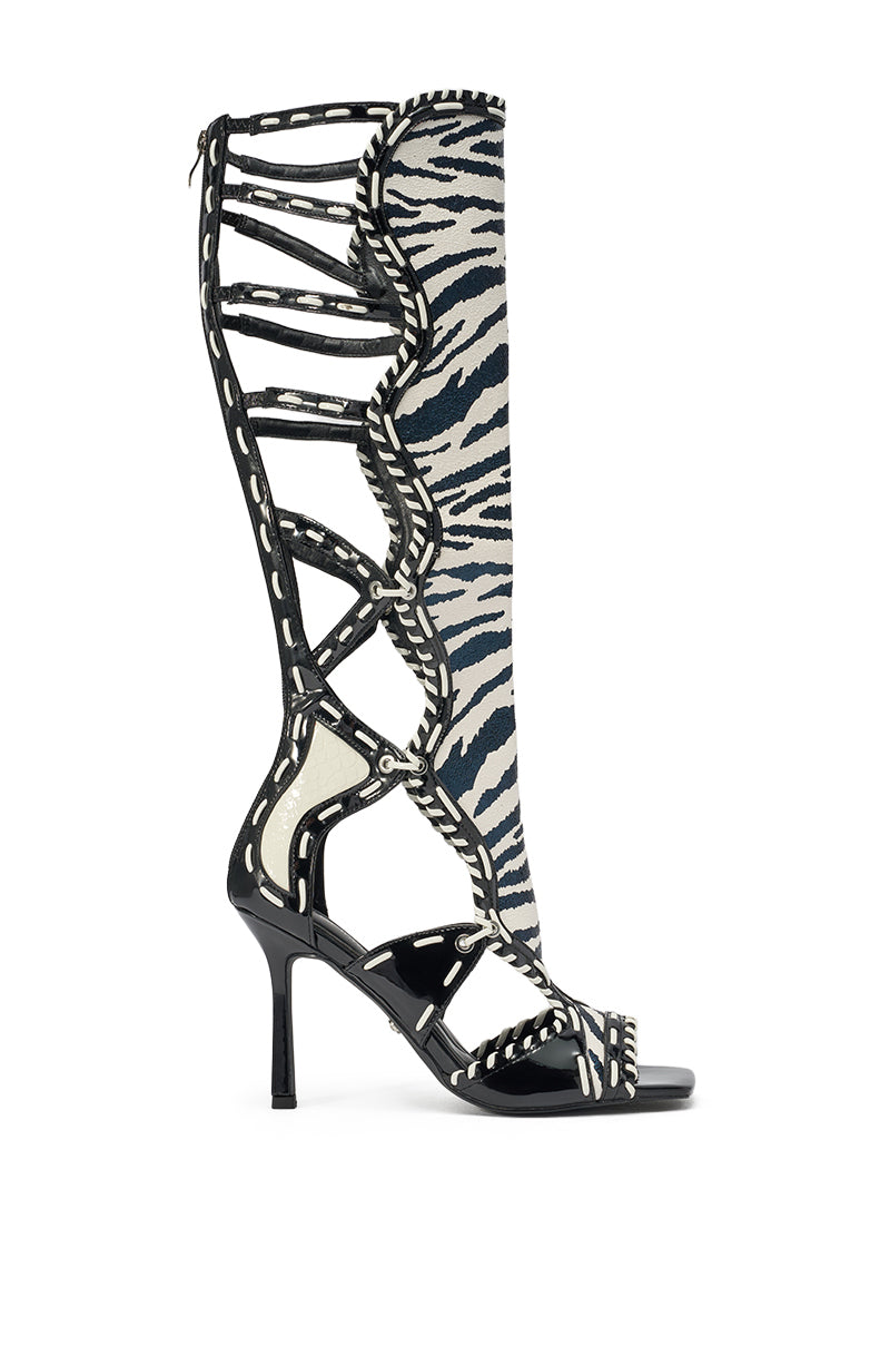 The AZALEA WANG INDRANI HIGH SHAFT BLACK AND WHITE ZEBRA PRINT GLADIATOR SANDAL is a knee-high, open-toe stiletto with cut-out sides, decorative stitching, and scalloped trim in a striking zebra pattern. 3