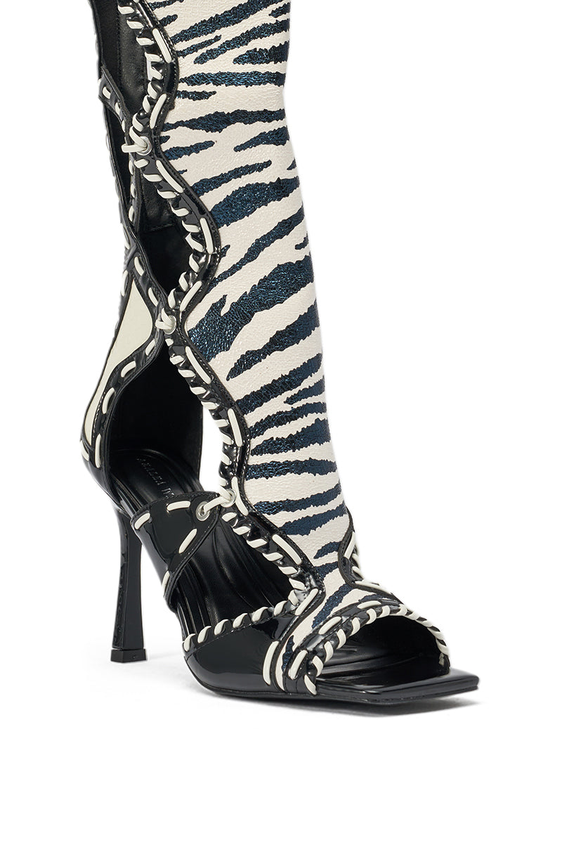 The AZALEA WANG INDRANI HIGH SHAFT BLACK AND WHITE ZEBRA PRINT GLADIATOR SANDAL features a stiletto heel, open toe, decorative stitching, and intricate cutout details for a striking look. 6