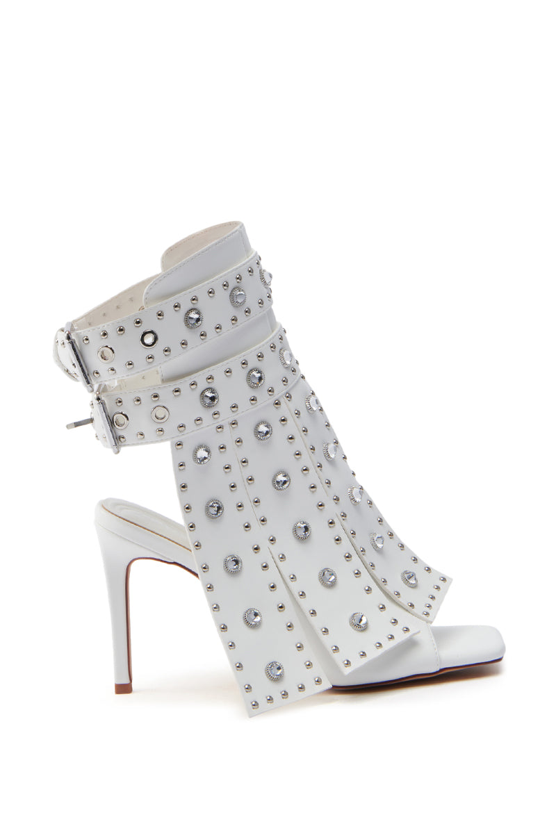 The AZALEA WANG IRELYN WHITE EMBELLISHED SANDAL features fringe-like straps, silver studs and crystal embellishments, an open toe, a stiletto heel for added height, and a wide ankle strap with a silver buckle for an edgy yet luxurious look.