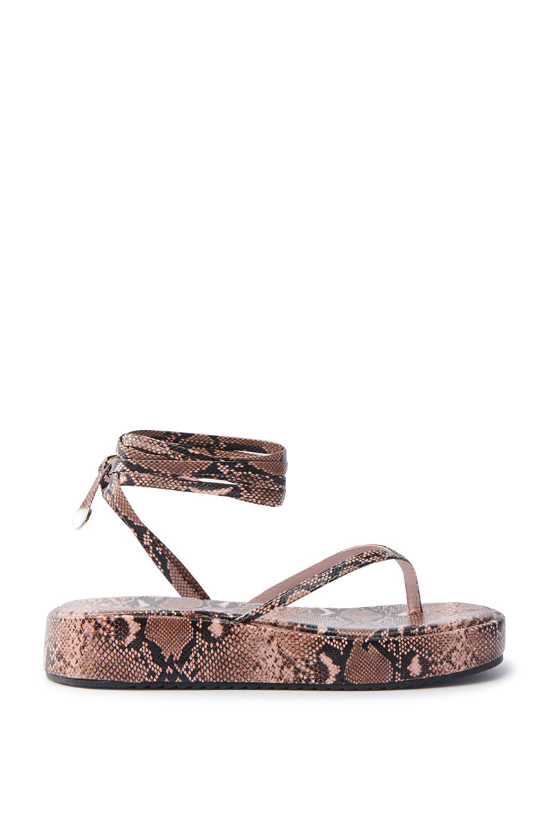 The AKIRA IRVINE BROWN SNAKE LACE UP FLAT SANDAL features a brown snake print with a flatform sole, thong strap, and pointed-tip ankle wrap. Made from faux leather, it's elegantly stylish for casual wear.
