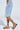 Wearing a light blue ripped denim skirt with a pearl chain, paired with the AKIRA IRVINE BROWN SNAKE LACE UP FLAT SANDAL, a person stands against a light grey background.