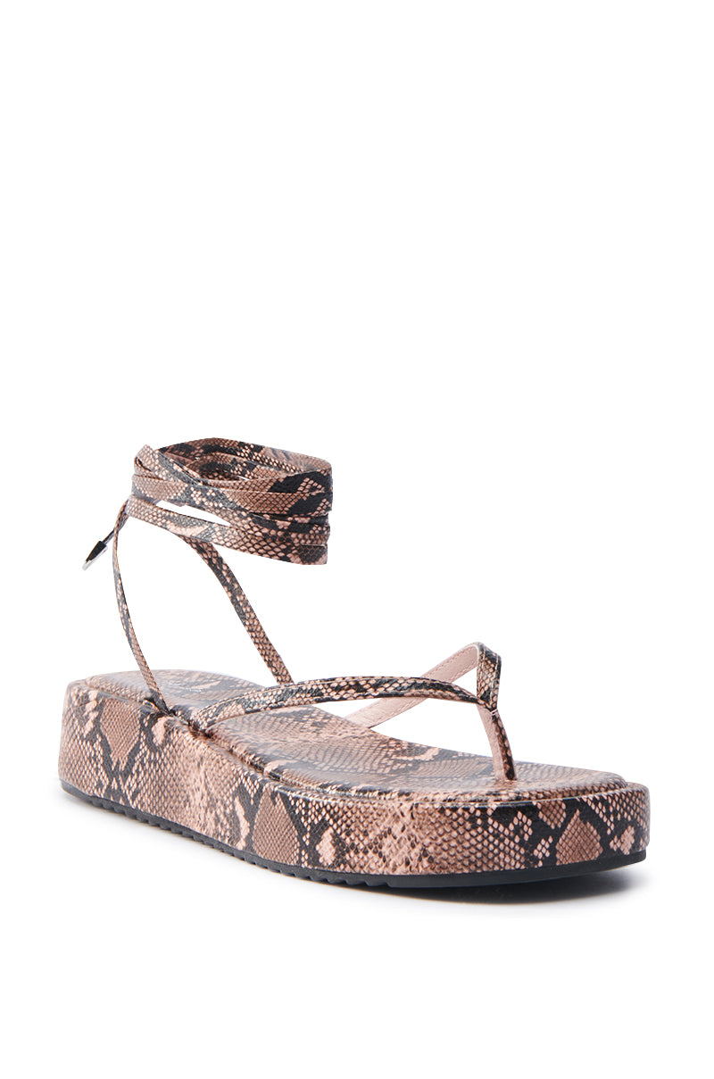 Introducing the AKIRA IRVINE BROWN SNAKE LACE UP FLAT SANDAL, with faux leather in a brown and black snakeskin pattern. It features a trendy flatform sole, chic ankle wrap straps, and a texture that mimics snake scales for a stylish appearance.