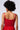 A person with curly hair is seen from the back, wearing the dazzling POP STAR HOT FIX RHINESTONE CROP TOP IN RED from the AKIRA Label. They have a delicate gold chain necklace with a small pendant and appear to be standing against a plain light background.