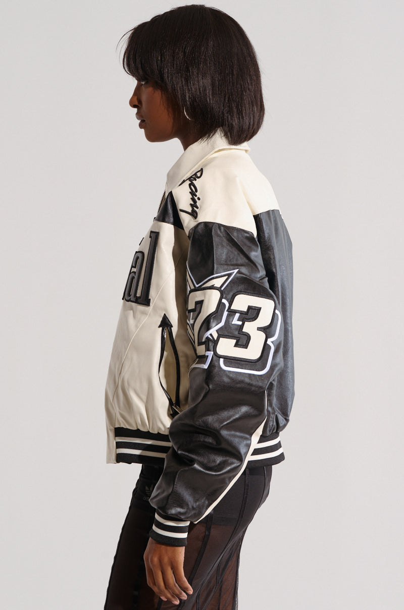 A person with medium-length dark hair wearing the ON THE RUN MOTO BOMBER stands sideways. The jacket, from the AKIRA Label Moto Bomber collection, features a mix of faux leather and fabric materials with racing-inspired patches, including the number "73" on the sleeve. The background is plain and light-colored.