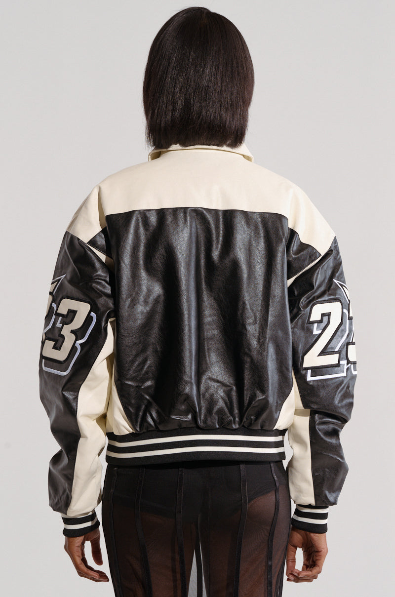 A person with straight, shoulder-length hair is shown from the back wearing an ON THE RUN MOTO BOMBER in black and white. Embroidered with the number "23" on both sleeves in a racing-inspired style, the varsity jacket complements sheer material making up the lower half of their outfit.