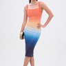 A woman stands confidently in the SUNSET LOVERS OMBRE MIDI DRESS, its gradient fading from orange to dark blue. The bodycon fit flatters her figure as she accessorizes with a clutch, gold chain-strap heels, and wears her hair in a high ponytail.