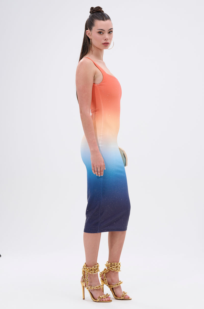 A woman with long dark hair in a high ponytail models the SUNSET LOVERS OMBRE MIDI DRESS and gold high-heeled sandals, standing sideways against a plain white background.