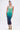 A woman poses against a plain background in the UNDER THE SEA RHINESTONE OMBRE MIDI DRESS, which fades from green to dark blue. She styles it with a high ponytail and green-yellow heels for a striking bodycon look.