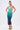 A woman poses with hands on hips in the UNDER THE SEA RHINESTONE OMBRE MIDI DRESS, featuring a light green to dark blue fade. She accessorizes with hoop earrings, green floral-accented heels, and a high ponytail.