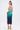 A woman with dark hair in a high ponytail models the UNDER THE SEA RHINESTONE OMBRE MIDI DRESS and yellow embellished high-heeled sandals, standing against a plain white background.