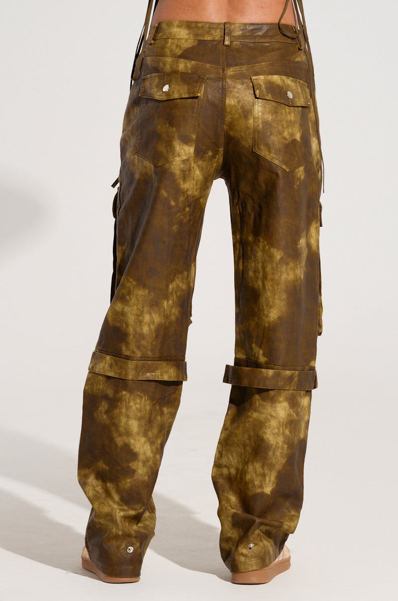 A person is seen from the back wearing the OUT LIKE A BANDIT FAUX LEATHER CARGO PANT, showcasing a brown tie-dye appearance with a distressed finish. These pants are designed with wide legs, adjustable knee straps, and a high-rise waist for enhanced style and comfort.