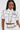 A woman wears the BLANK SPACE CROPPED SHORT SLEEVE BUTTON DOWN, a pop-art inspired white shirt with black outlines and "BLANK" on the pocket, paired with matching high-waisted pants, standing against a plain light background.