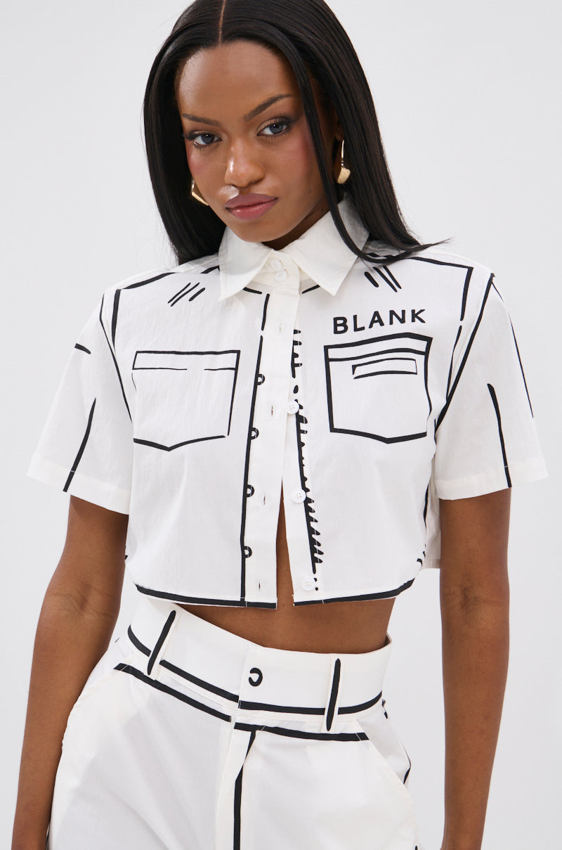 A woman wears the BLANK SPACE CROPPED SHORT SLEEVE BUTTON DOWN, a white pop-art-inspired shirt with bold black line designs that mimic drawn-on seams and pockets, featuring "BLANK" printed above the left chest pocket.
