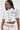 A woman wears the BLANK SPACE Cropped Short Sleeve Button Down, a white pop-art shirt with bold black outlines, faux pockets, and "BLANK" on the left chest, paired with matching high-waisted pants.
