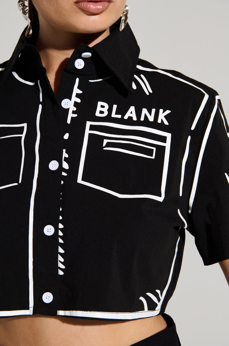 A close-up view of a person wearing the BLANK SPACE BUTTON DOWN CROP SHIRT from AKIRA Label, featuring a black button-up design with white outlines resembling pockets and a collar. The shirt is adorned with a graphic sketch-inspired print and the word "BLANK" on the upper left side. The person is also accessorized with hoop earrings.