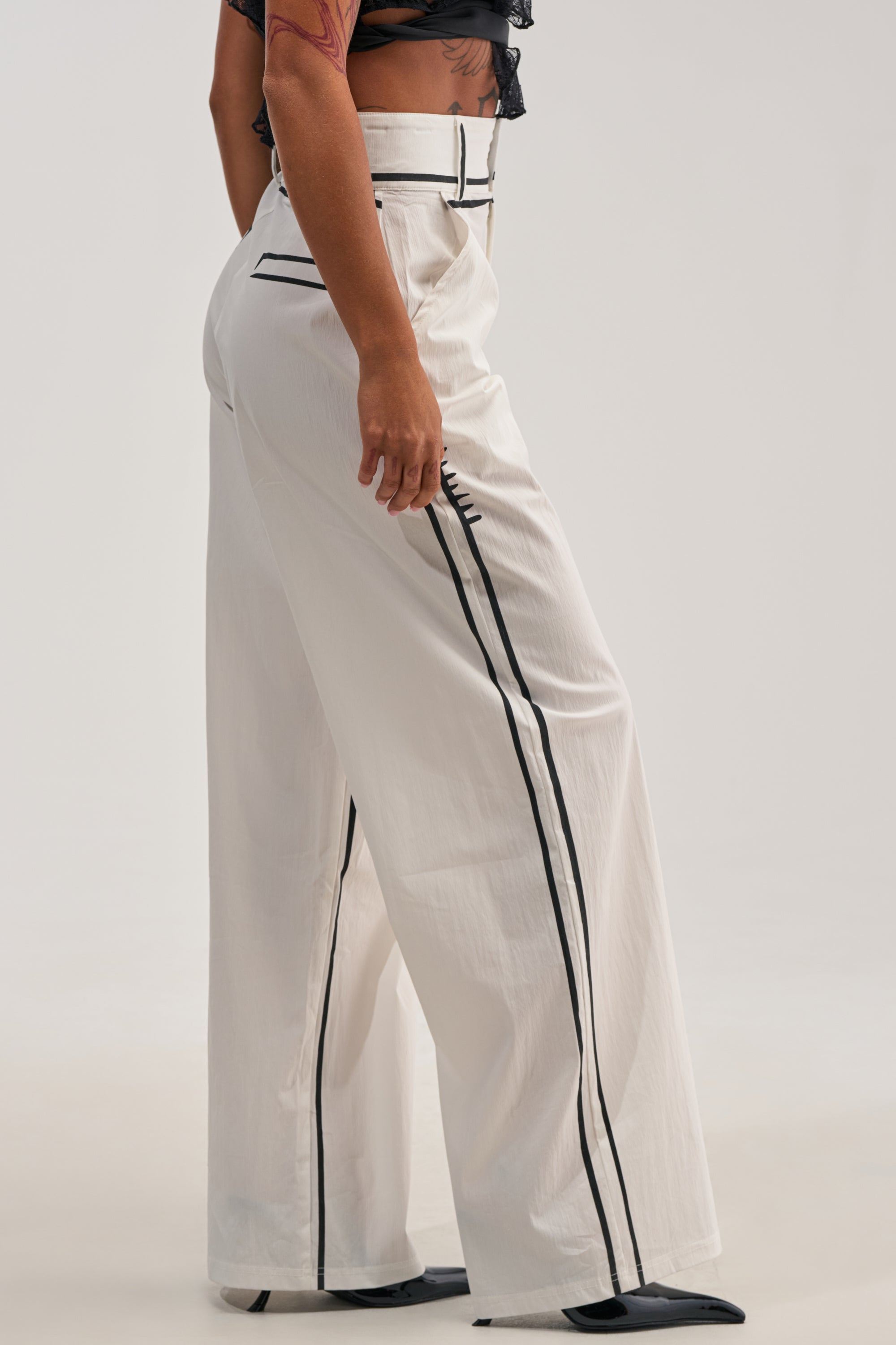 Wearing the BLANK SPACE HIGH WAIST PALAZZO PANT featuring white fabric and striking black stripe details, paired with black pointed shoes. The dramatic wide-leg silhouette brings bold concert energy to the look. Only the lower body is visible against a plain, light background.