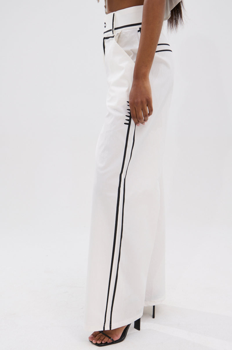 A person wearing the BLANK SPACE HIGH WAIST PALAZZO PANT with black vertical piping and black high-heeled sandals, shown in side view against a white background, highlights the chic wide-leg silhouette for minimalist style.